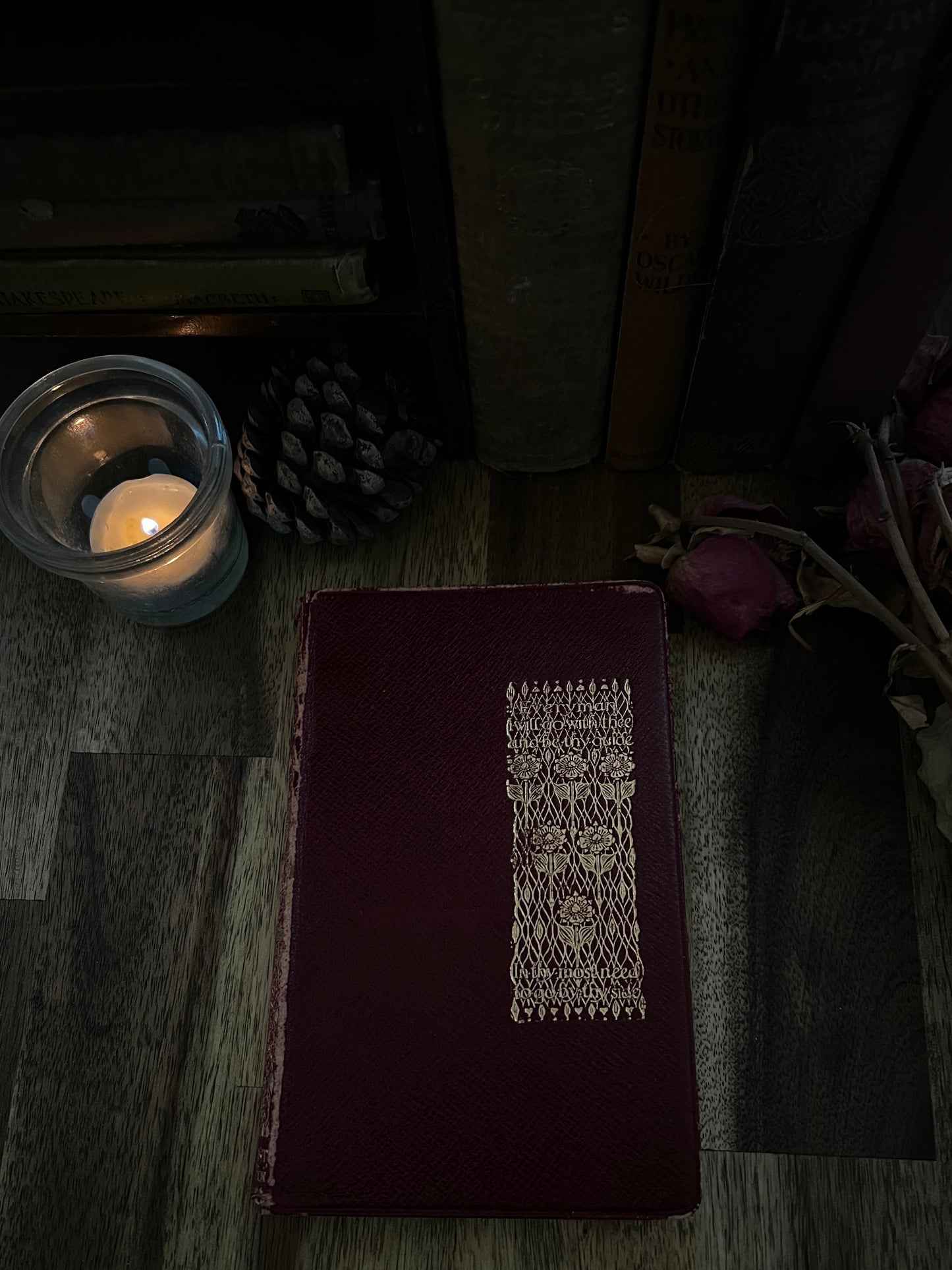 Dark brown leather-bound book with intricate design on a wooden surface with a lit candle.