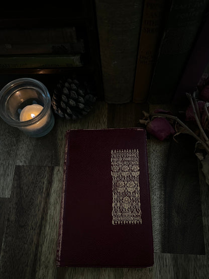 Dark brown leather-bound book with intricate design on a wooden surface with a lit candle.